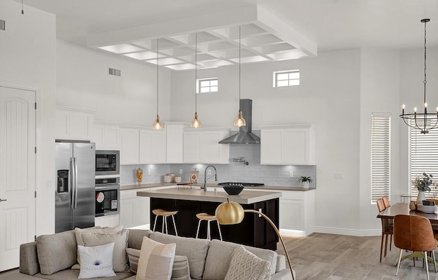 kitchen with wall chimney exhaust hood, white cabinetry, appliances with stainless steel finishes, an island with sink, and decorative backsplash