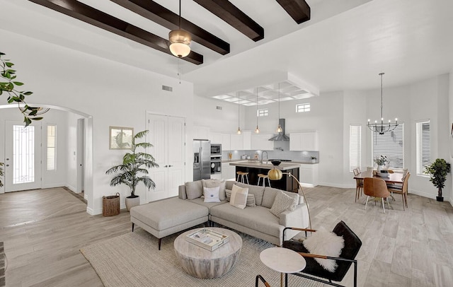 living room with a towering ceiling, beam ceiling, light hardwood / wood-style flooring, and a notable chandelier