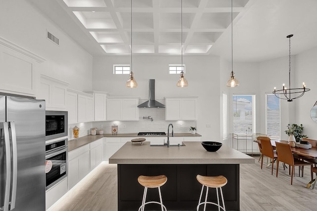 kitchen with tasteful backsplash, appliances with stainless steel finishes, wall chimney range hood, a kitchen island with sink, and white cabinets