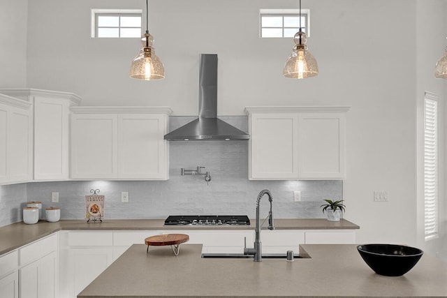 kitchen featuring decorative light fixtures, stainless steel gas stovetop, white cabinetry, decorative backsplash, and wall chimney exhaust hood