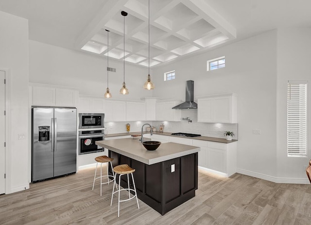 kitchen with appliances with stainless steel finishes, a kitchen island with sink, white cabinets, and wall chimney exhaust hood