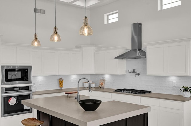 kitchen featuring white cabinetry, appliances with stainless steel finishes, hanging light fixtures, and wall chimney range hood