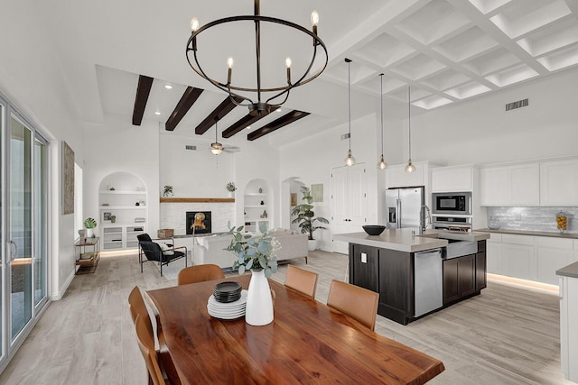 dining room with beam ceiling, ceiling fan with notable chandelier, built in features, and light hardwood / wood-style flooring