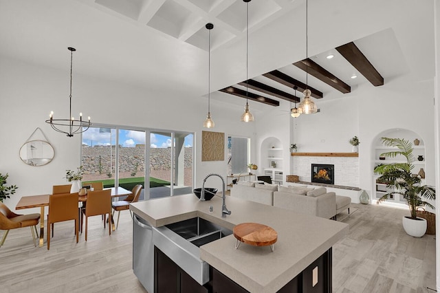 kitchen featuring a stone fireplace, pendant lighting, beamed ceiling, an island with sink, and built in shelves