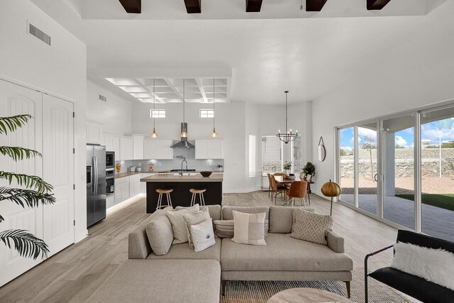 living room with a chandelier, a high ceiling, coffered ceiling, light hardwood / wood-style floors, and beam ceiling