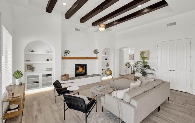 living room featuring built in shelves, a towering ceiling, beam ceiling, and light wood-type flooring