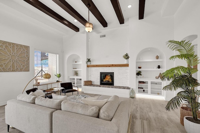 living room with a brick fireplace, beam ceiling, built in features, and light wood-type flooring