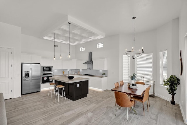 kitchen featuring wall chimney range hood, decorative light fixtures, black appliances, and a center island with sink