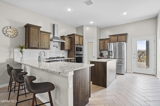 kitchen featuring light parquet floors, kitchen peninsula, stainless steel appliances, wall chimney exhaust hood, and sink