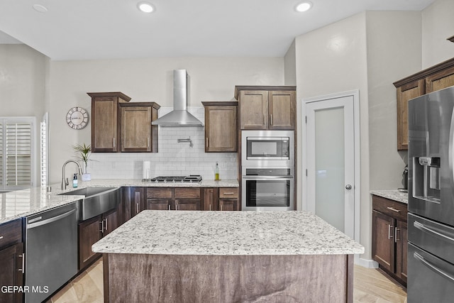 kitchen featuring appliances with stainless steel finishes, decorative backsplash, wall chimney range hood, a kitchen island, and sink