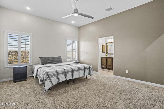 bedroom featuring ceiling fan, light colored carpet, multiple windows, and ensuite bathroom