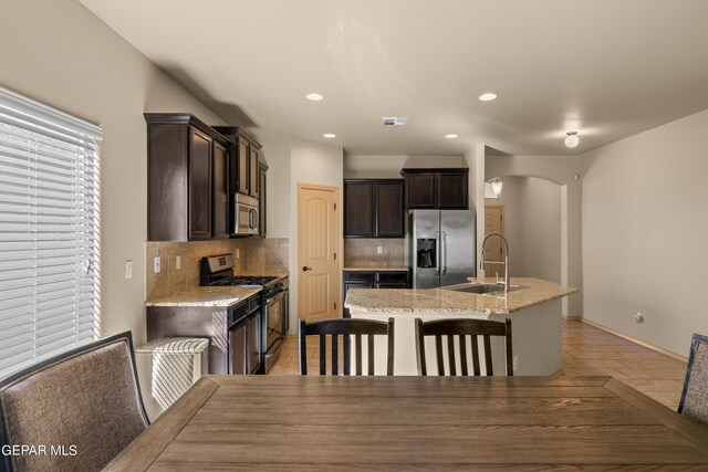 kitchen with an island with sink, dark brown cabinetry, backsplash, sink, and appliances with stainless steel finishes