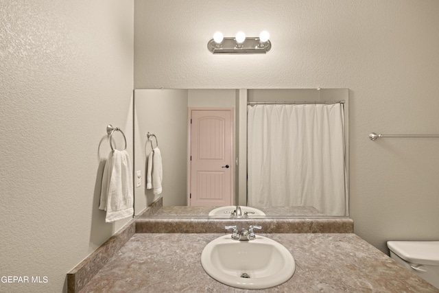 bathroom with a shower with shower curtain, a textured wall, vanity, and toilet