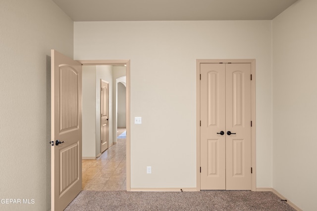 unfurnished bedroom featuring light carpet, baseboards, and a closet