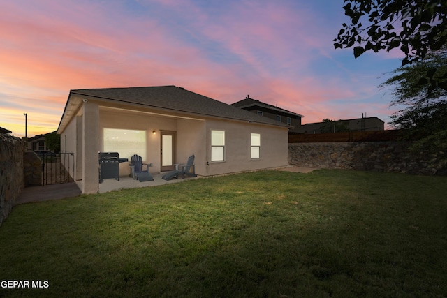 back of house at dusk featuring a patio, a lawn, a fenced backyard, and stucco siding