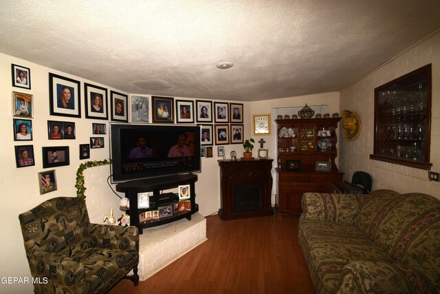 living room featuring a textured ceiling, a fireplace, wood-type flooring, and brick wall