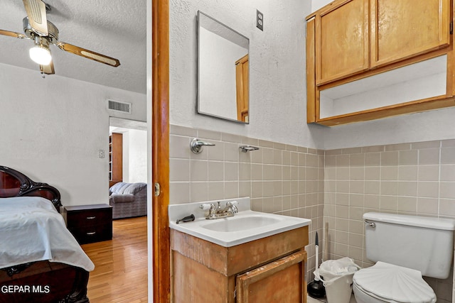 bathroom with hardwood / wood-style floors, a textured ceiling, toilet, vanity, and tile walls