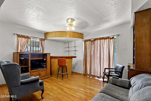 living room featuring ceiling fan, light hardwood / wood-style flooring, and a textured ceiling