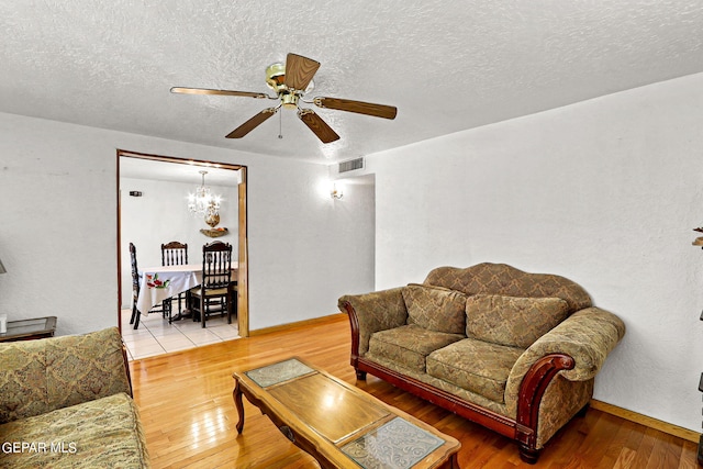 living room with ceiling fan with notable chandelier, a textured ceiling, and light hardwood / wood-style flooring