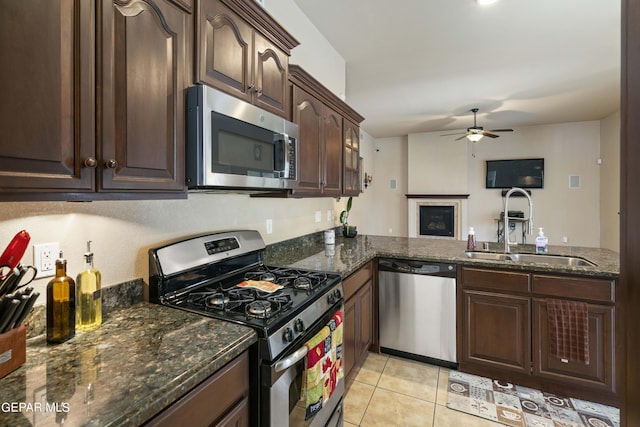 kitchen with ceiling fan, sink, dark stone counters, light tile patterned floors, and stainless steel appliances