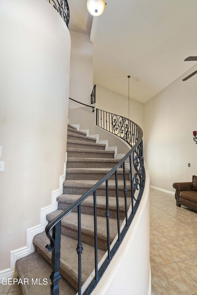 stairway featuring a towering ceiling, tile patterned floors, and ceiling fan