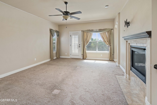 unfurnished living room with ceiling fan, light colored carpet, and a tiled fireplace