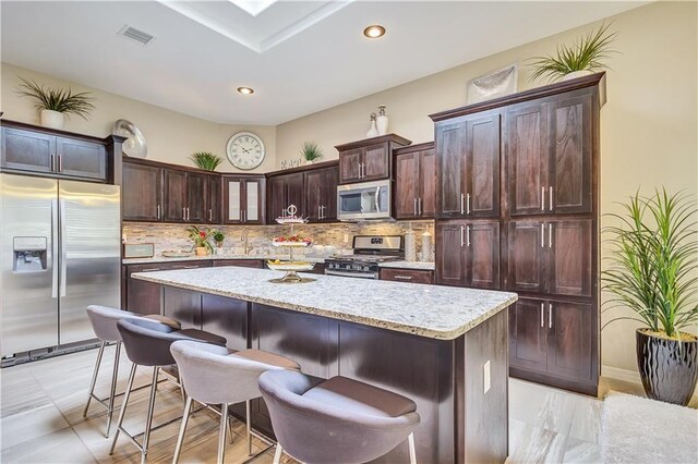 1701 Bull Ring St, El Paso, TX 79928 - kitchen with appliances with stainless steel finishes, tasteful backsplash, a kitchen island, light stone counters, and dark brown cabinetry