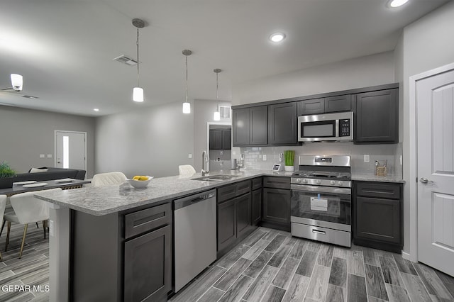 kitchen with tasteful backsplash, appliances with stainless steel finishes, kitchen peninsula, pendant lighting, and light stone countertops