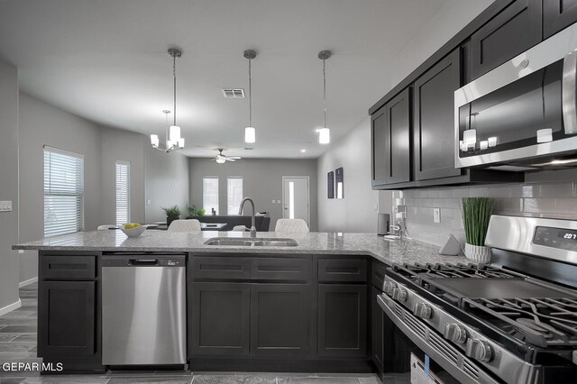 kitchen with sink, appliances with stainless steel finishes, backsplash, light stone countertops, and decorative light fixtures