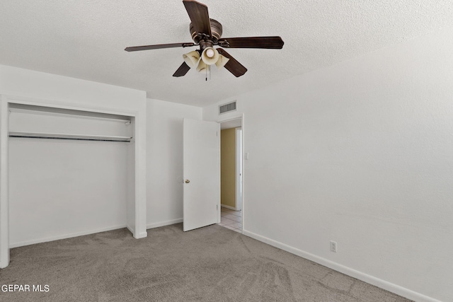 unfurnished bedroom featuring light carpet, a textured ceiling, a closet, and ceiling fan