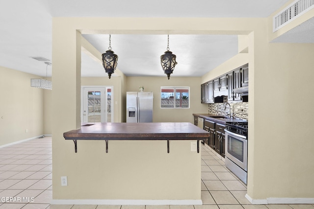 kitchen featuring backsplash, sink, light tile patterned floors, a kitchen bar, and stainless steel appliances