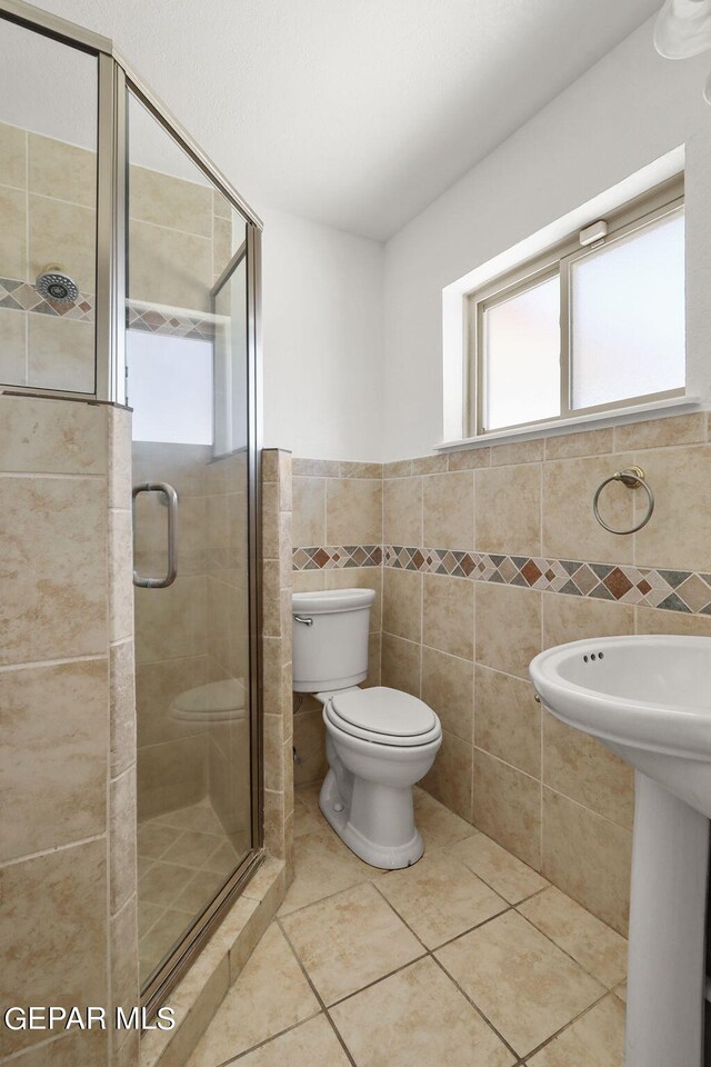 bathroom with tile patterned flooring, toilet, tile walls, and an enclosed shower