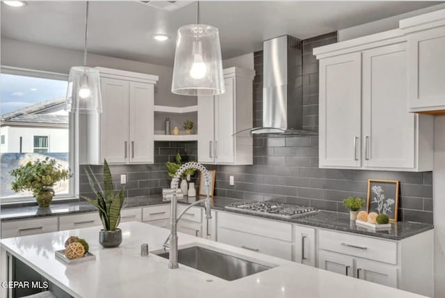 kitchen with backsplash, stainless steel gas cooktop, wall chimney exhaust hood, and decorative light fixtures