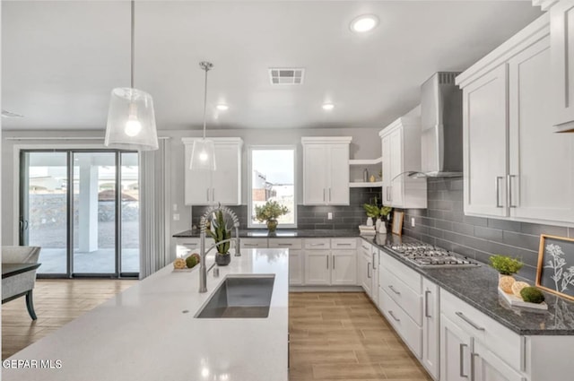 kitchen featuring wall chimney range hood, decorative backsplash, and white cabinets