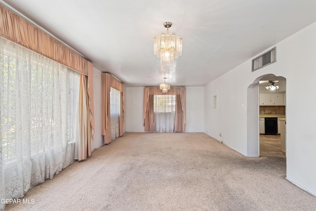 carpeted spare room with arched walkways, visible vents, and a notable chandelier