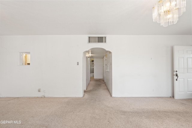 carpeted empty room with visible vents, arched walkways, and a chandelier