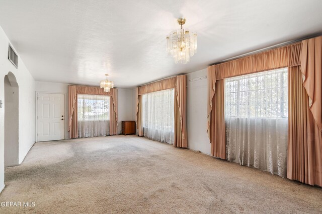 carpeted spare room featuring a chandelier