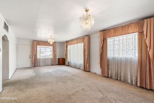 carpeted spare room featuring visible vents, a chandelier, and arched walkways