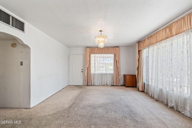 spare room featuring light carpet and a chandelier