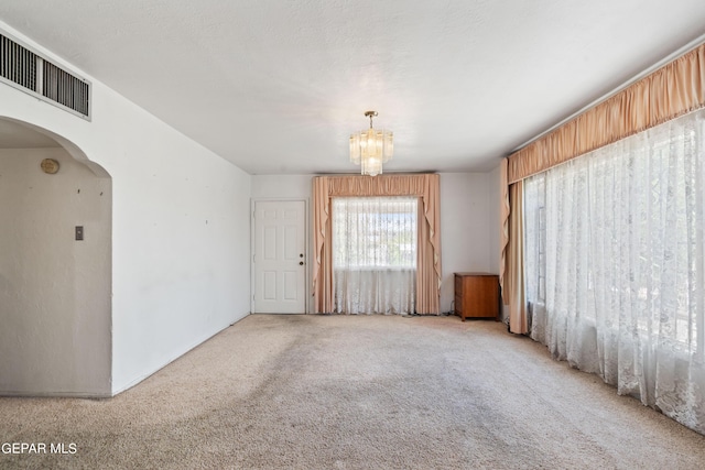 empty room with arched walkways, a textured ceiling, a notable chandelier, carpet flooring, and visible vents