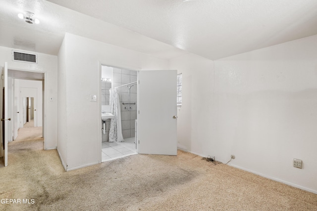 unfurnished bedroom featuring ensuite bathroom, carpet floors, a textured ceiling, and visible vents