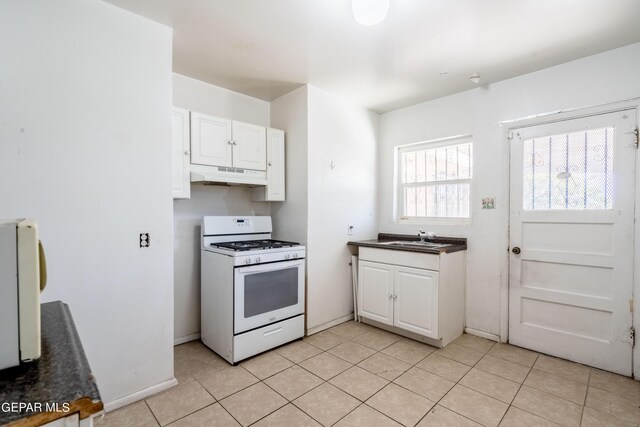 kitchen with white gas stove, white cabinets, light tile patterned floors, and sink