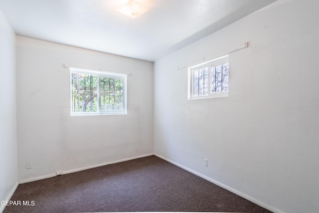 unfurnished room with dark carpet, a wealth of natural light, and baseboards