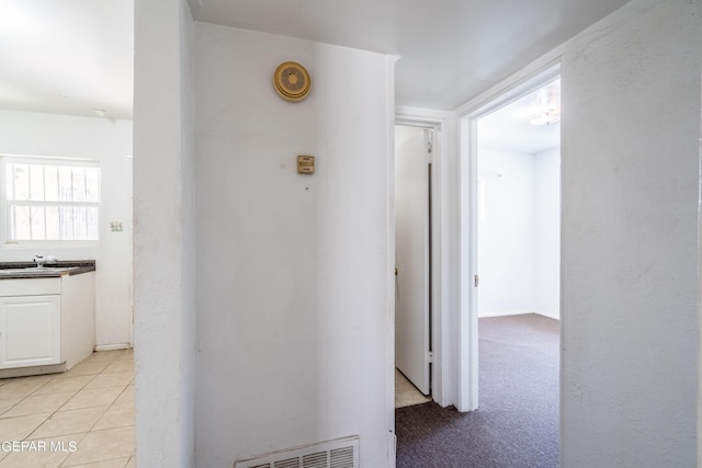 corridor with light colored carpet, visible vents, and light tile patterned floors