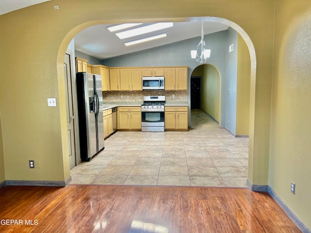 kitchen with light brown cabinetry, vaulted ceiling with skylight, appliances with stainless steel finishes, and light hardwood / wood-style flooring