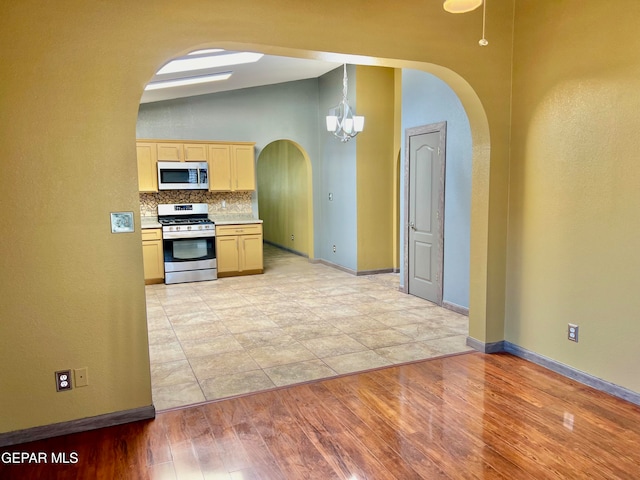 kitchen featuring stainless steel appliances, light wood-type flooring, lofted ceiling, light brown cabinetry, and a chandelier