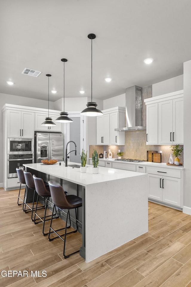 12741 Eltham Dr, Horizon City, TX 79928 - kitchen with a large island, visible vents, wall chimney exhaust hood, stainless steel appliances, and white cabinetry