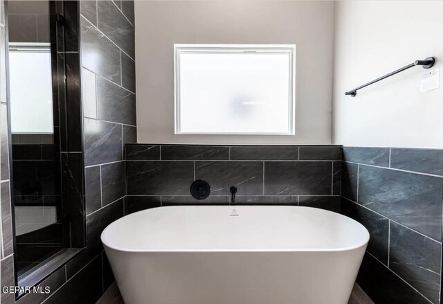 bathroom featuring plus walk in shower and tile walls