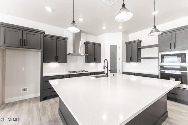 kitchen with decorative light fixtures, wall chimney range hood, oven, sink, and black microwave