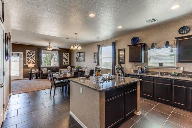 kitchen featuring ceiling fan with notable chandelier, a kitchen island, dark brown cabinetry, a textured ceiling, and dark tile patterned flooring